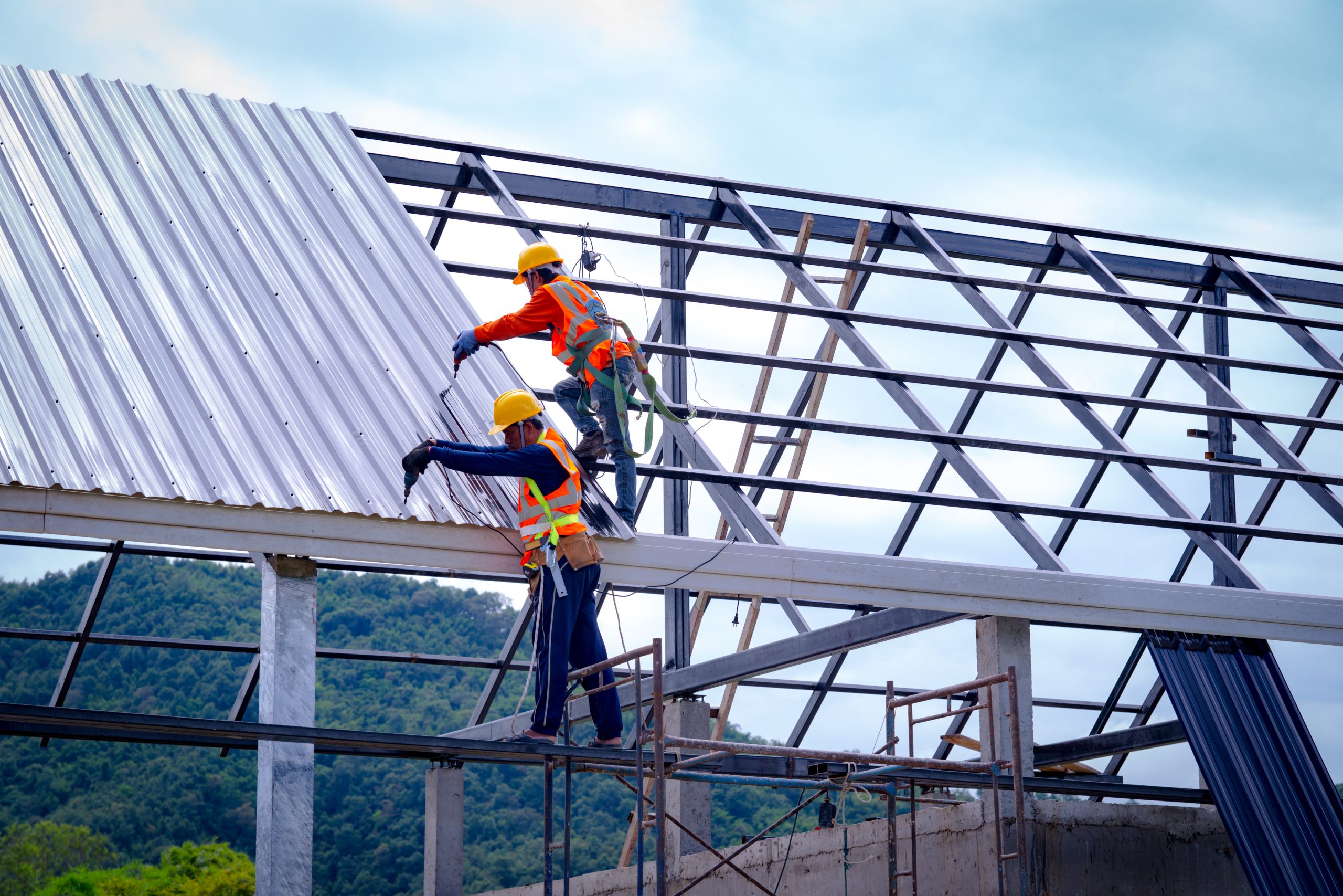 Roofer worker in protective uniform wear and gloves, using air or pneumatic nail gun and installing asphalt shingle on top of the new roof,Concept of residential building under construction.