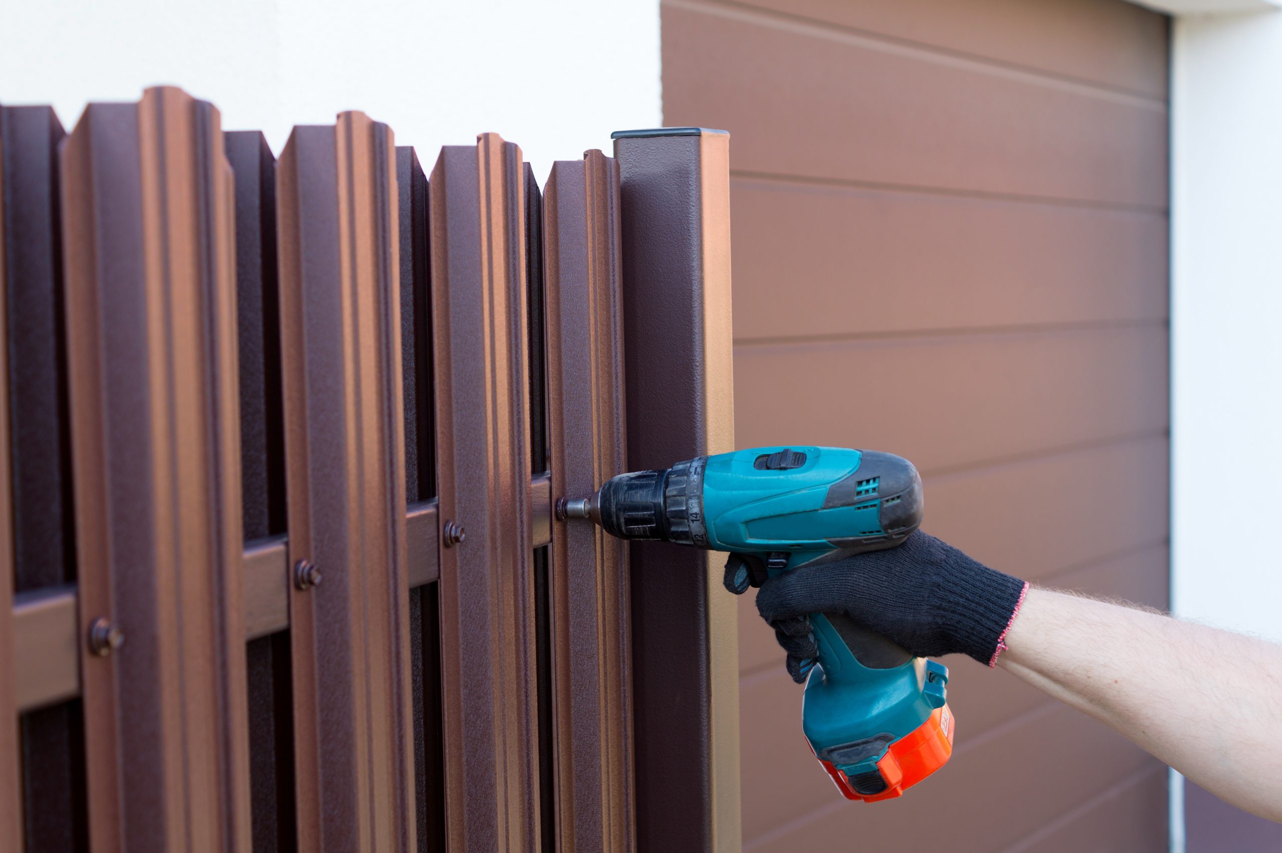 Screwing roofing screws into a metal picket fence by using cordless electric screwdriver. Fencing, installing the fence. Close up.